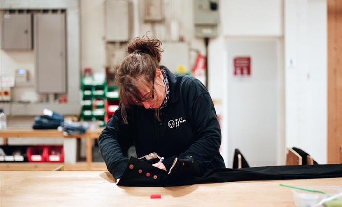 A Hiut Denim Grandmaster carefully signs a pair of finished jeans on a large wooden worktable. She’s focused on the details, reflecting the brand’s de